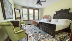 A bedroom with a wooden bed, a green armchair, a desk, a radiator, and a large window. - Knit Inn.. (Frostburg)