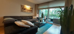 Un salon moderne avec un canapé foncé, une table basse et une grande fenêtre donnant sur un paysage verdoyant.