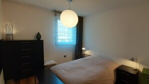 A bedroom with a bed, a dresser, a nightstand, a lamp, and a window with blinds. - Very nice apartment downtown, Parc Olympe de Gouges ( with garage) (Annemasse)