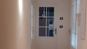 A hallway with wooden flooring, a white door with a window, and a wall-mounted light fixture. - Very nice apartment downtown, Parc Olympe de Gouges ( with garage) (Annemasse)