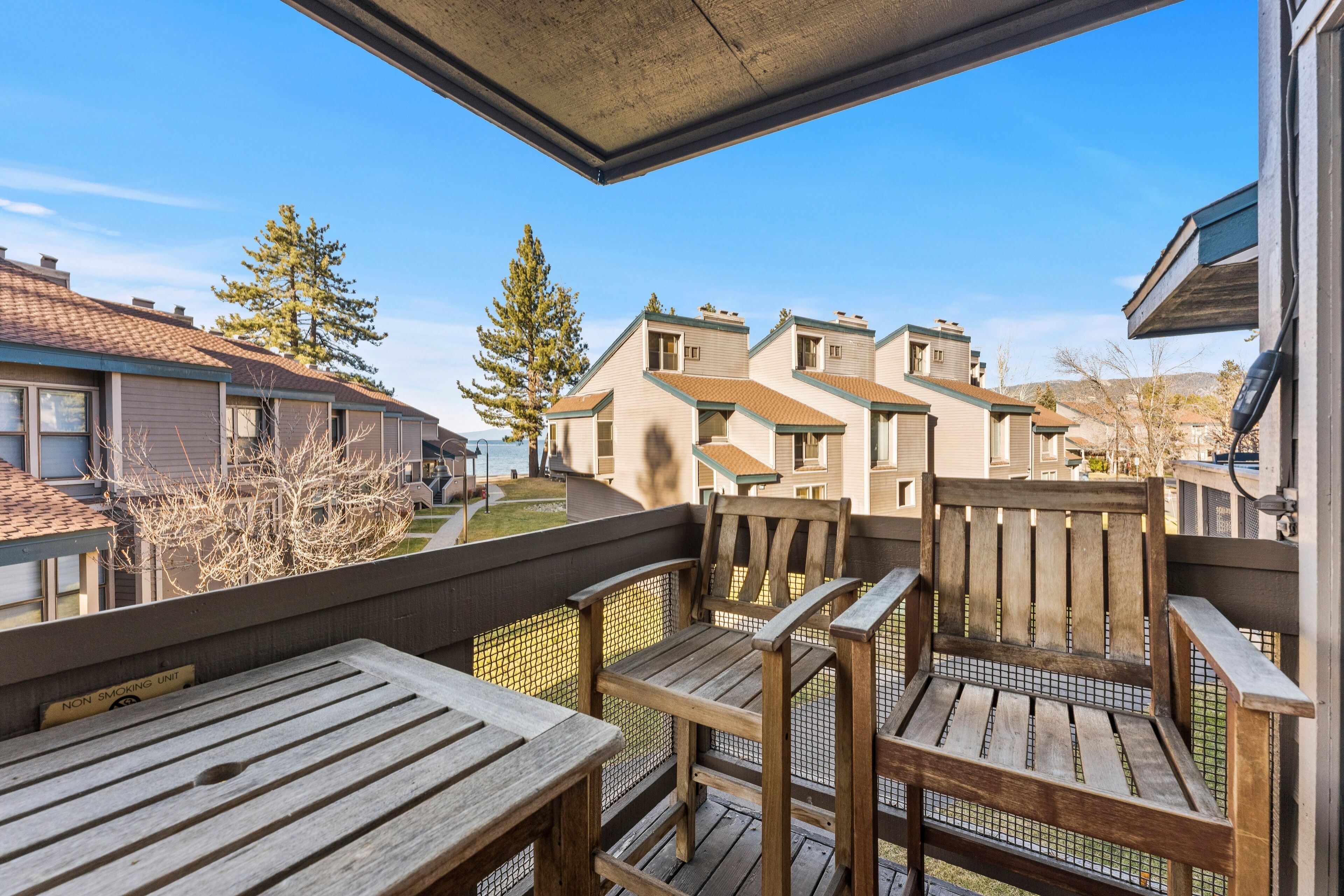 A balcony with wooden chairs and tables, overlooking a residential area with houses and trees.