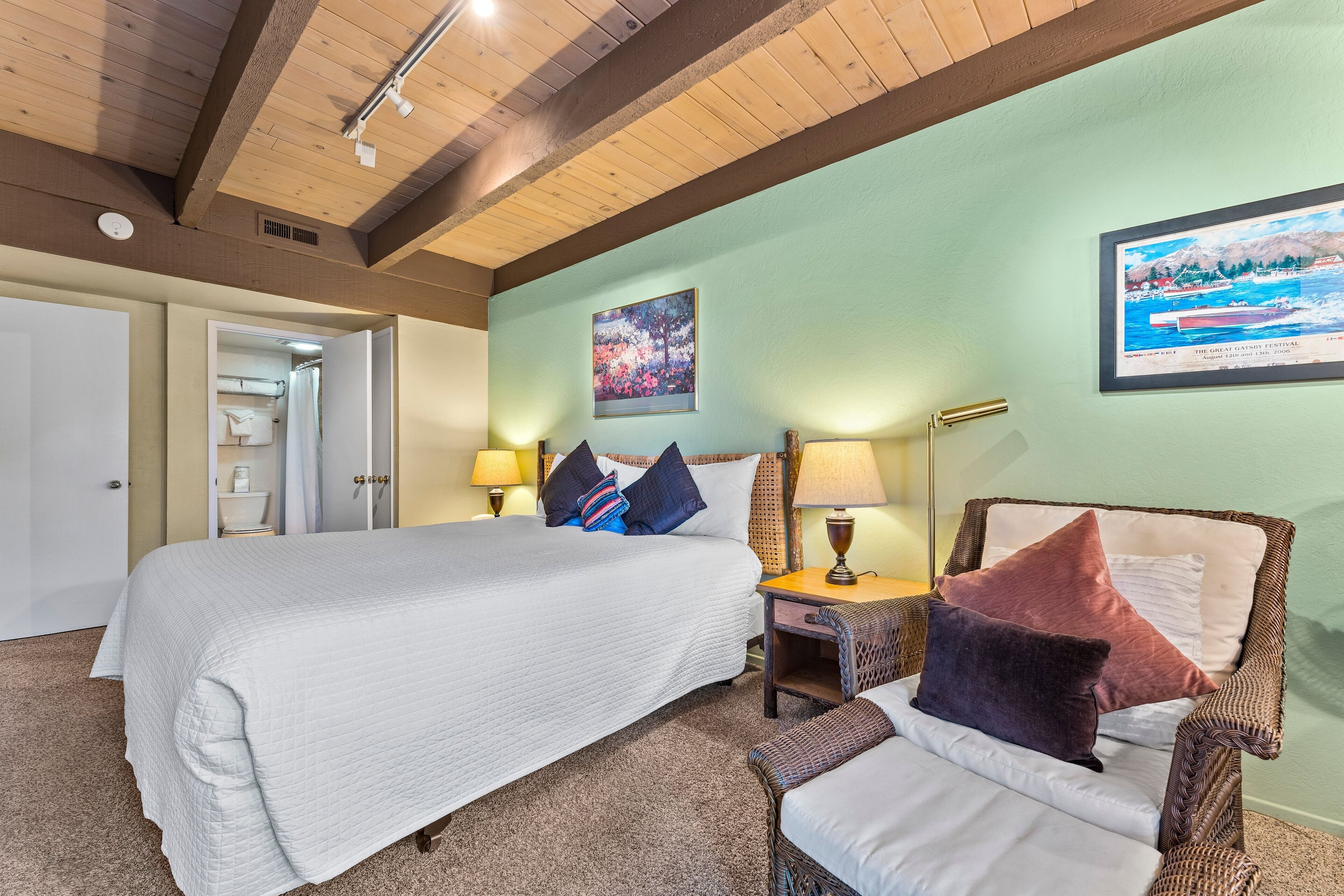 A bedroom with a large bed, a chair, a nightstand, and a wall-mounted lamp.
