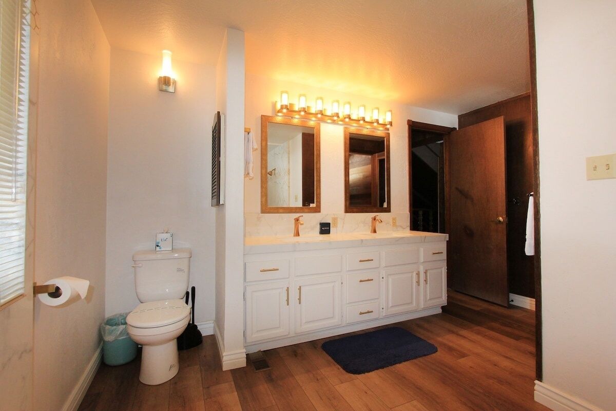 Une salle de bain avec des toilettes blanches, un meuble-lavabo double avec un miroir et un luminaire placé au-dessus du miroir.