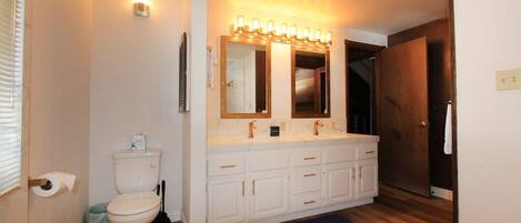 A bathroom with a white toilet, a double sink vanity with a mirror, and a light fixture above the mirror.