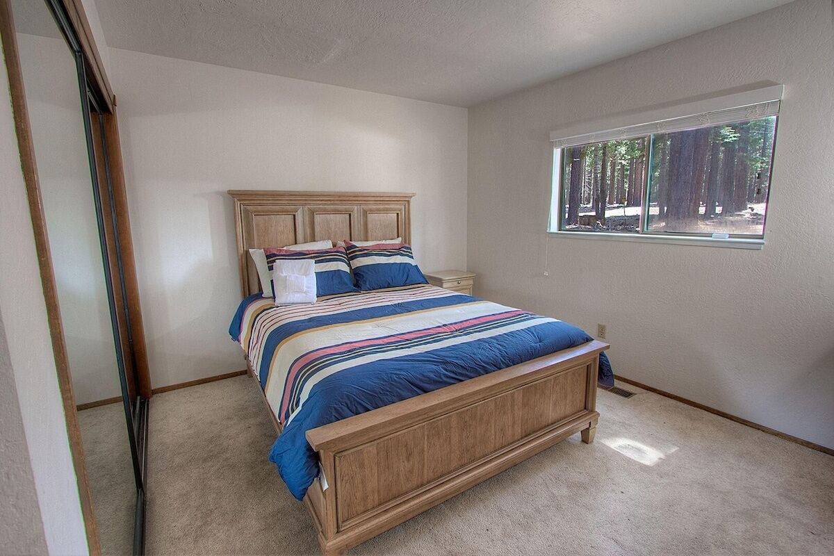 A bedroom with a wooden bed, a window with a view of trees, and a carpeted floor.