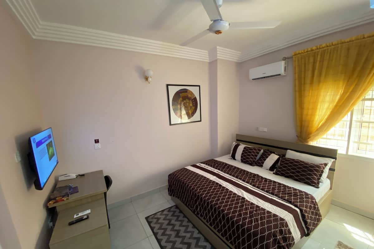 A bedroom with a bed, a desk, a ceiling fan, an air conditioner, and a window with curtains.