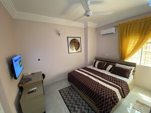 A bedroom with a bed, a desk, a ceiling fan, an air conditioner, and a window with curtains. - C7 Hazelwood Residence & Suites (Abuja)