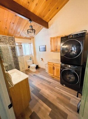 A compact kitchen with wooden cabinets, a double washer, a sink, and a stone backsplash. - Slope & Mountain Views! Walk to the Zoo and Slope Pick Up!  (Big Bear Lake)