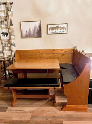 A wooden bench with a cushioned seat and backrest, a small table, and two framed pictures on the wall. - Slope & Mountain Views! Walk to the Zoo and Slope Pick Up!  (Big Bear Lake)