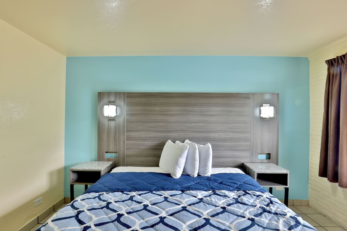 Ein Hotelzimmer mit einem Bett, zwei Nachttischen, einem Kopfteil und zwei Wandleuchten.