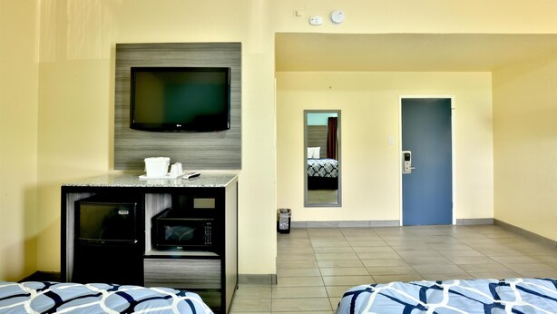 A hotel room with a TV, kitchenette, two beds, a mirror, and a door leading to the hallway. - Americas Best Value Inn San Antonio Airport South (San Antonio)