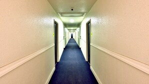 A long, narrow hallway with cream-colored walls and a dark blue carpet. - Americas Best Value Inn San Antonio Airport South (San Antonio)