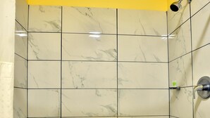 A shower with white marble tiles, a yellow ceiling, and a showerhead. - Americas Best Value Inn San Antonio Airport South (San Antonio)