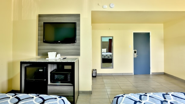 Ein Hotelzimmer mit Fernseher, Küchenzeile, zwei Betten, einem Spiegel und einer Tür zum Flur.