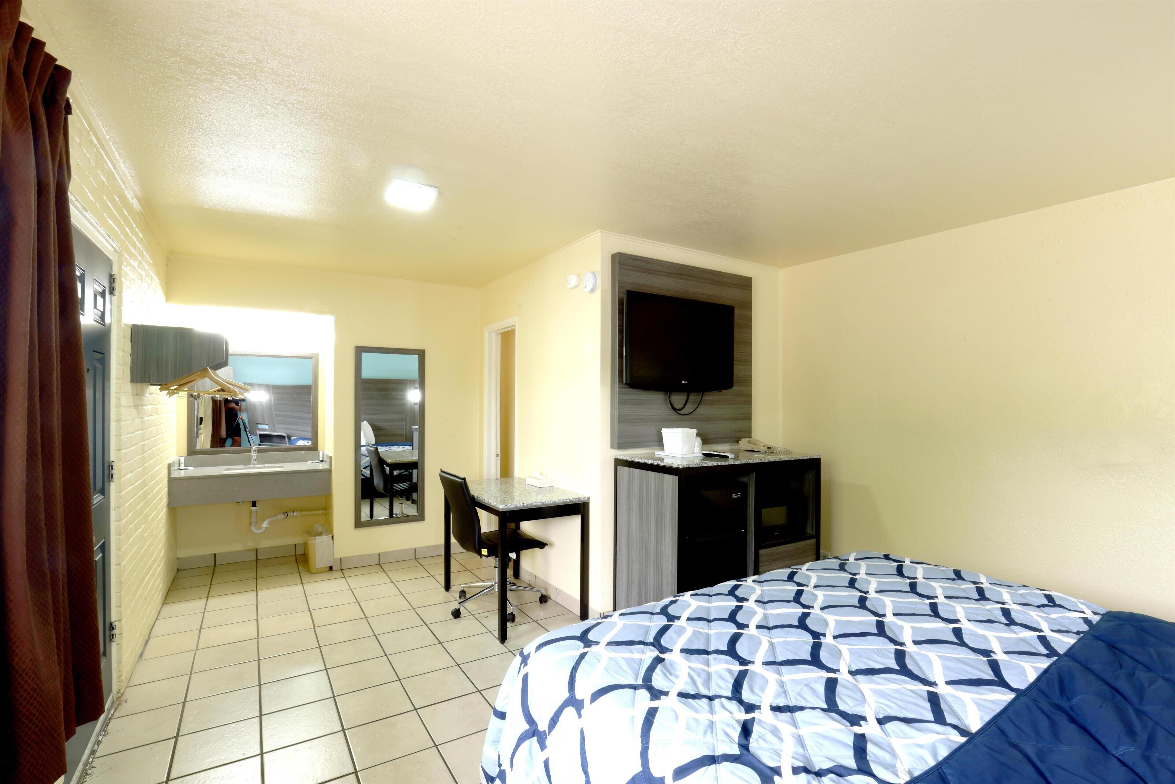 A hotel room with a bed, a desk, a chair, a television, and a bathroom with a mirror and sink.