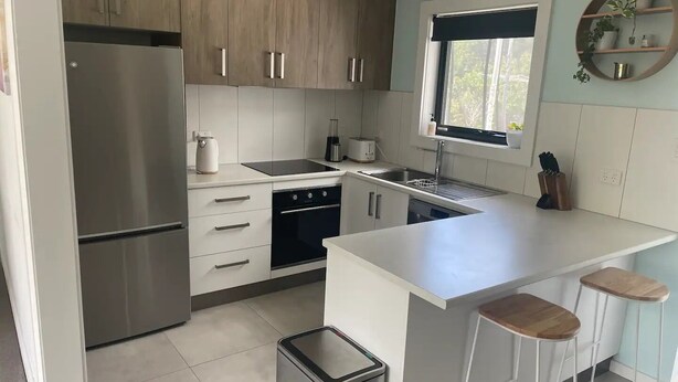 A modern kitchen with stainless steel appliances, white cabinetry, a window, and a bar stool area. - Little White House on Ecclestone close to city centre and Tamar Valley Wineries! (Riverside)