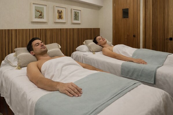 Deux lits avec des draps blancs et des couvertures bleu clair, des têtes de lit en bois et des œuvres d’art encadrées accrochées au mur.
