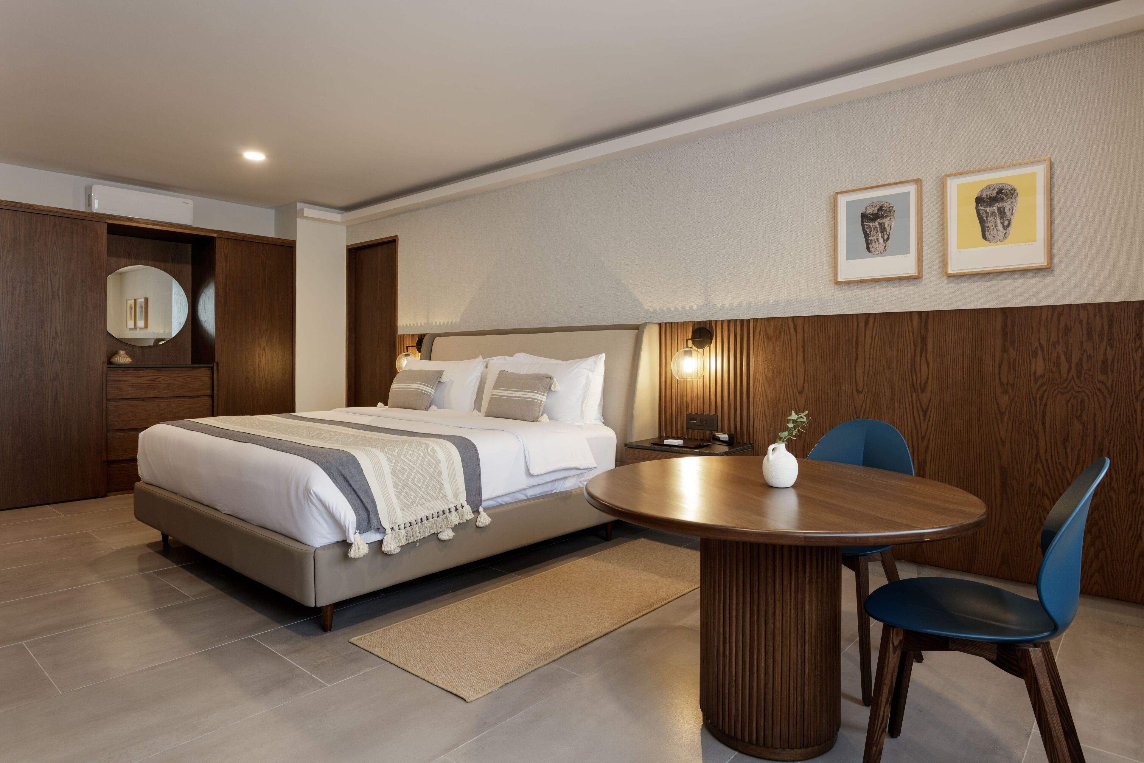 Una habitación de hotel moderna con una cama grande, una mesa de comedor redonda de madera y dos sillas.