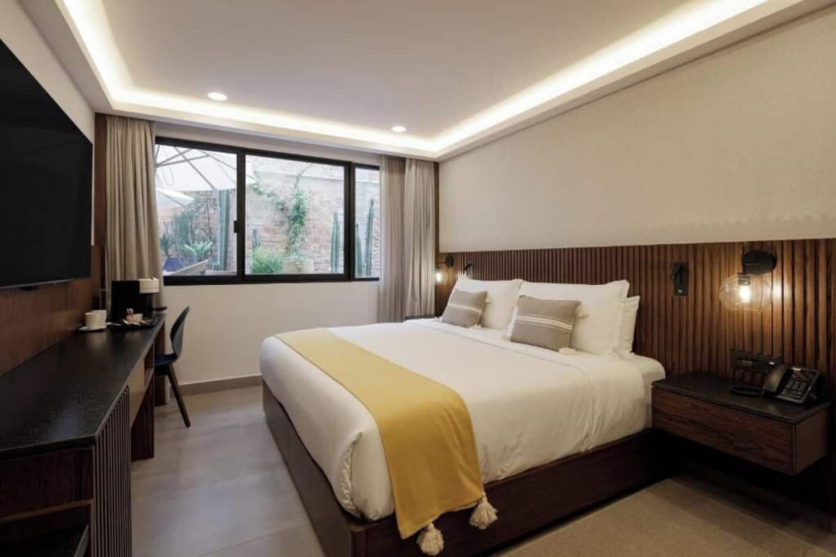 Une chambre d’hôtel avec un grand lit, un bureau, une chaise, une télévision et une fenêtre avec des rideaux.