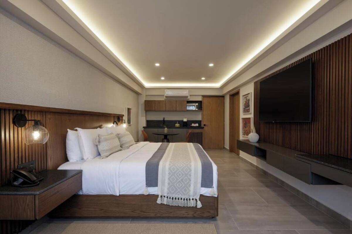 Une chambre d’hôtel moderne équipée d’un lit, d’une table de chevet, d’une lampe et d’un téléviseur à écran plat fixé au mur.