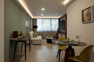 Una sala de estar moderna con sofá, mesa de comedor y sillas. Hay un televisor en la pared y una ventana con cortinas.
