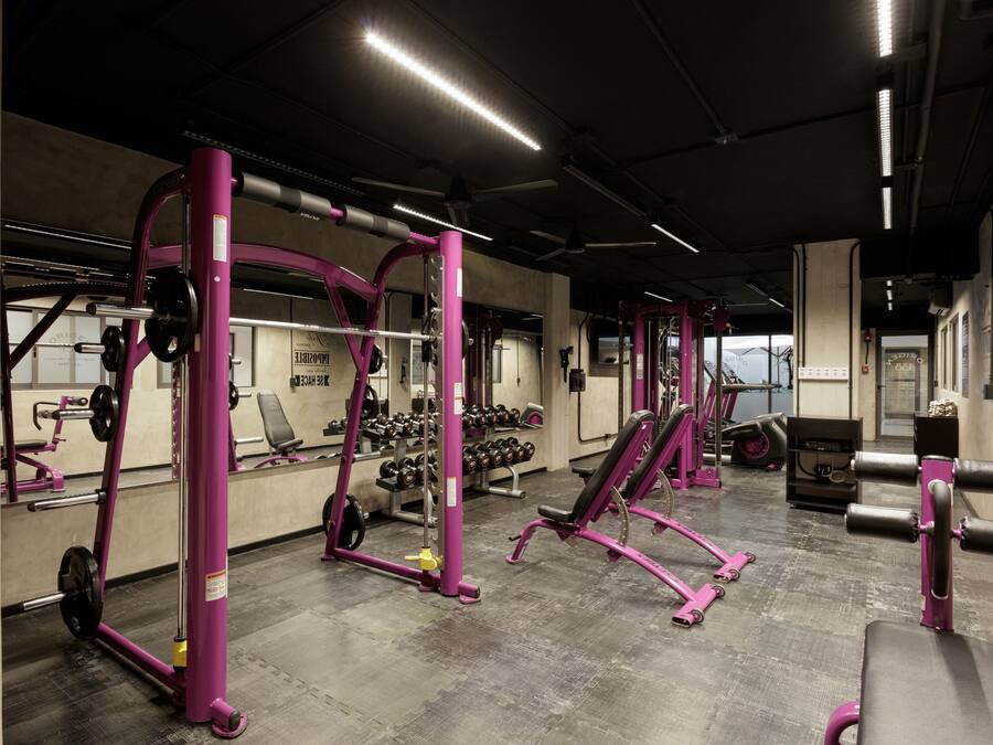 Un gimnasio con equipo púrpura, estantes para pesas y un espejo.