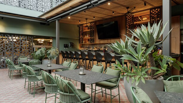 Ein Essbereich mit grünen Stühlen und Tischen, eine Bar mit Fernseher und eine Wand mit geometrischem Muster.