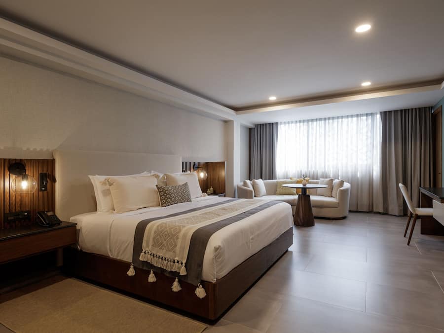 A modern hotel room with a large bed, a desk, a sofa, and a dining table.
