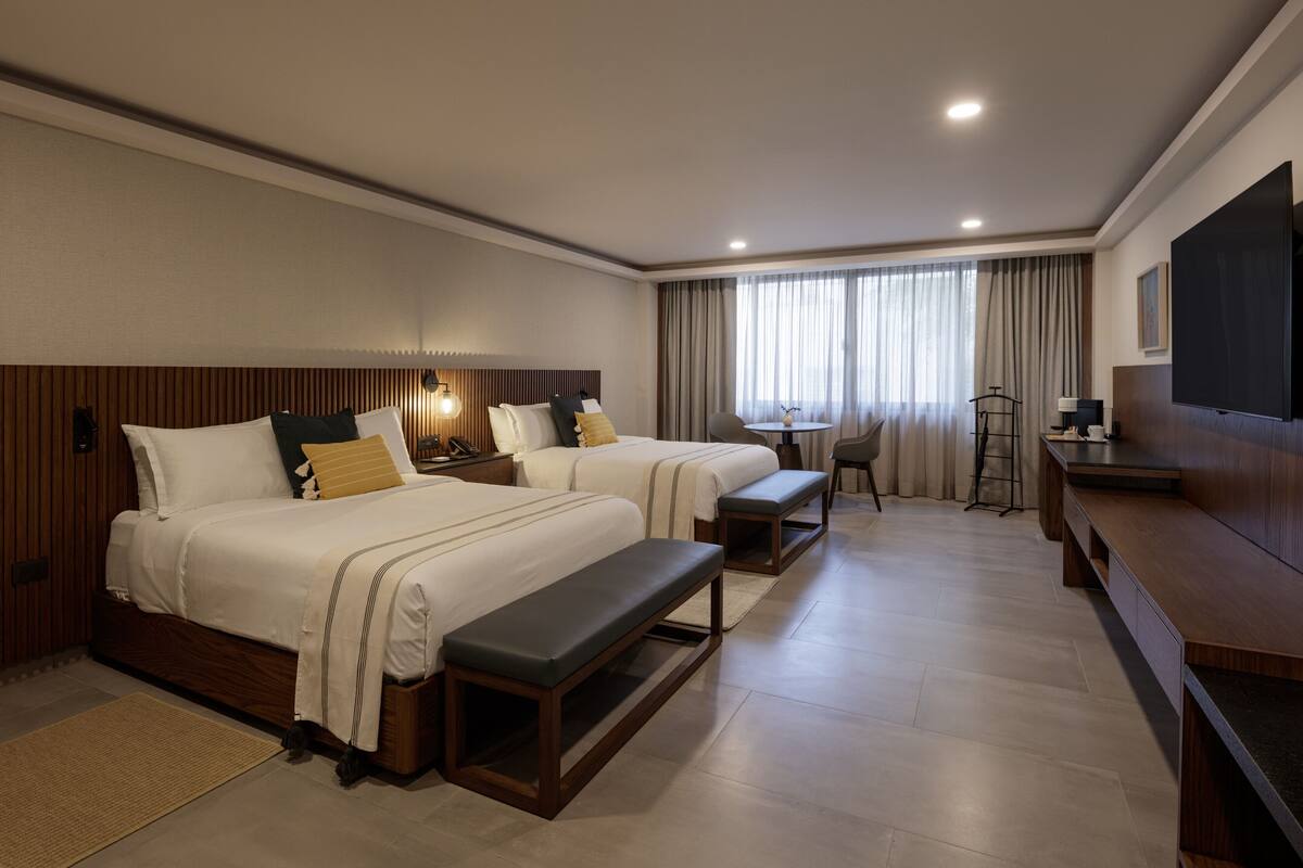 Une chambre d’hôtel avec deux lits, un bureau, une chaise et une télévision.