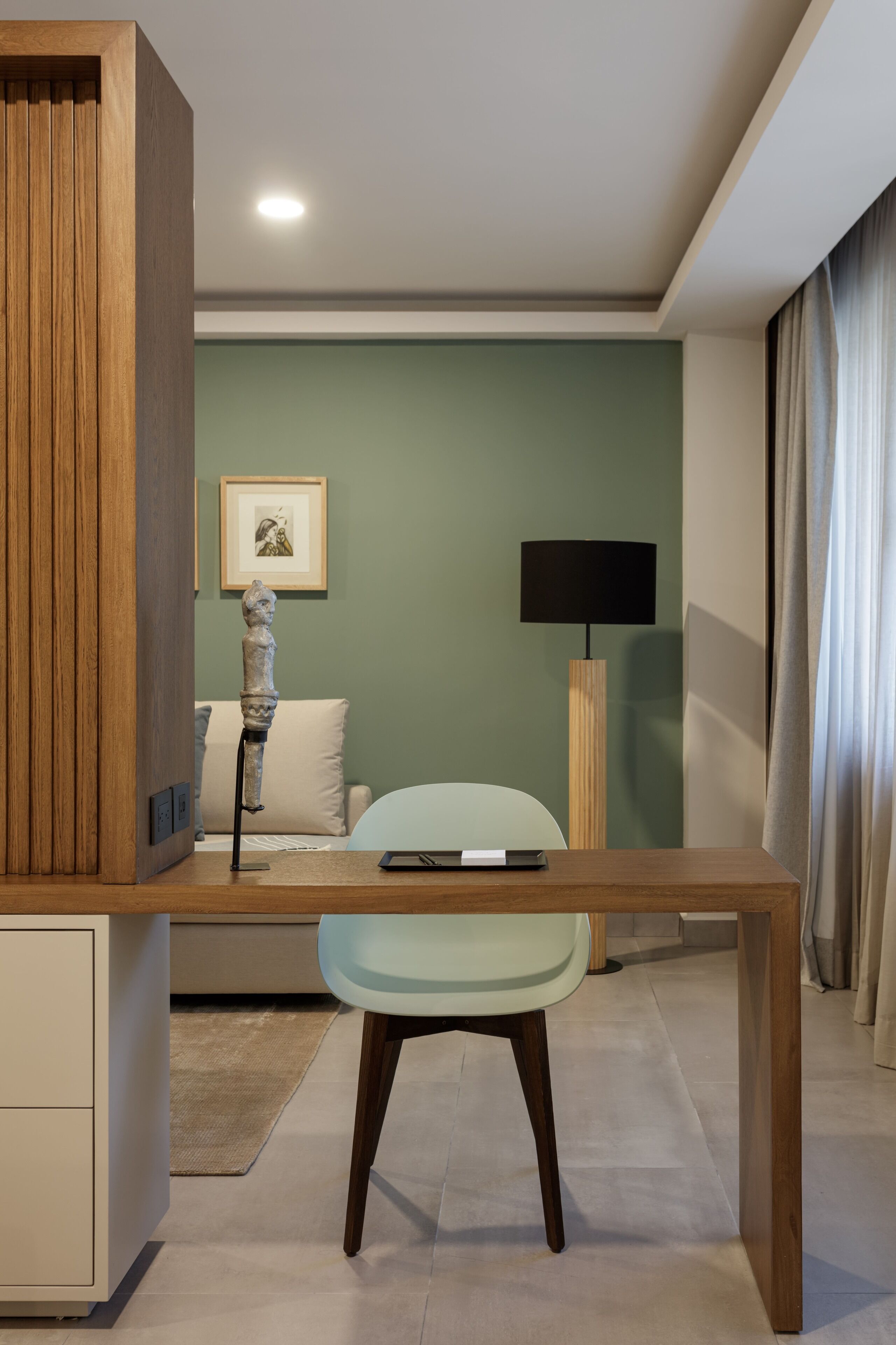 Una habitación moderna con un escritorio de madera, una silla verde clara, un sofá blanco, una lámpara de pie y un cuadro en la pared.