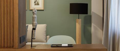 Una habitación moderna con un escritorio de madera, una silla verde clara, un sofá blanco, una lámpara de pie y un cuadro en la pared.