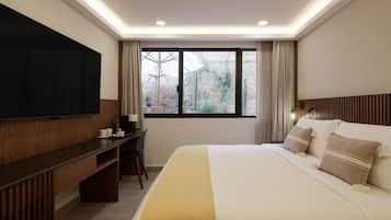 Habitación de hotel con una cama grande, televisor de pantalla plana, escritorio y ventana con cortinas.
