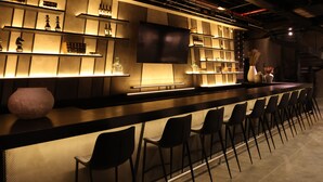 Eine Bar mit einer langen Theke, mehreren Regalen voller Flaschen und einigen Stühlen.
