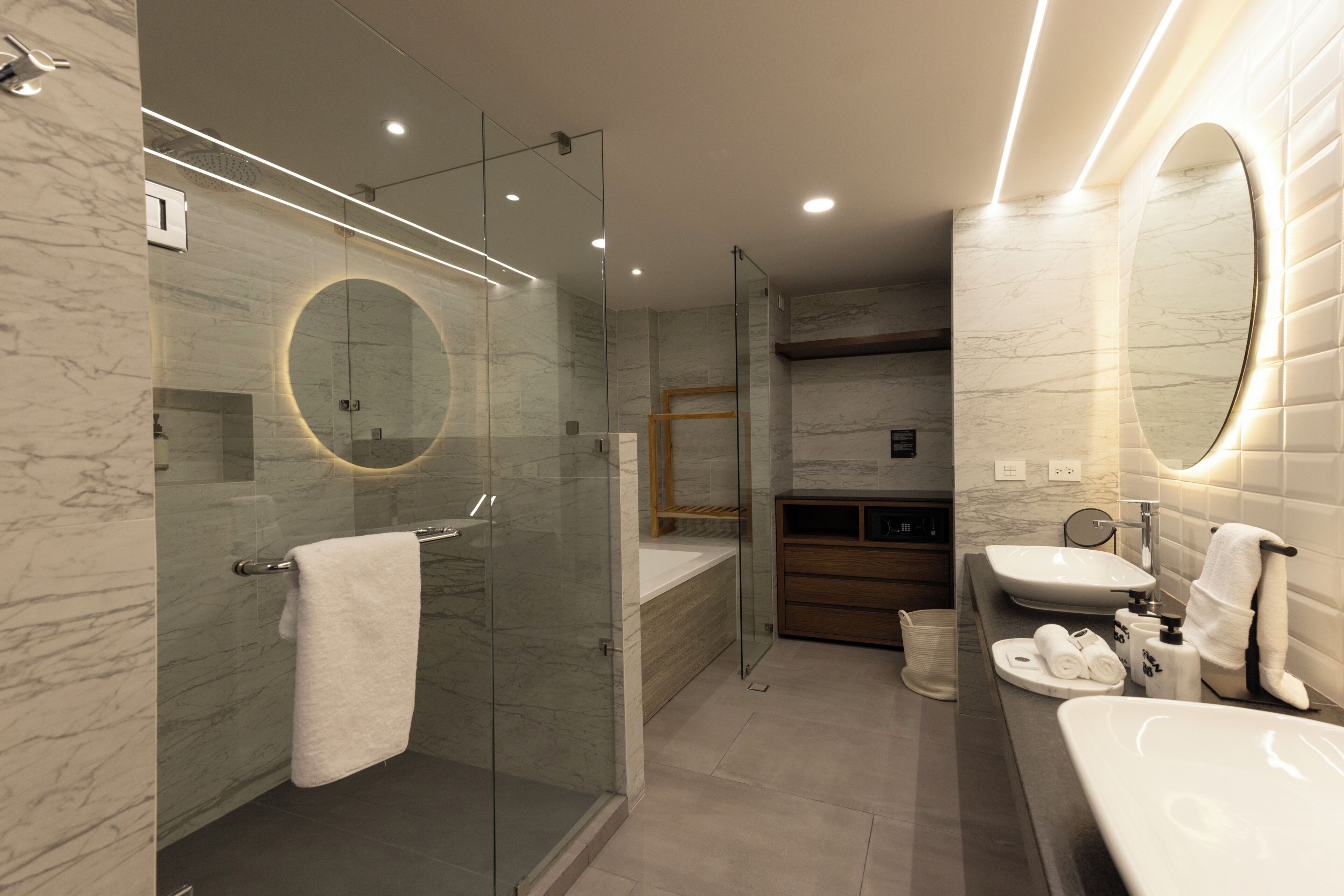 Un baño moderno con ducha envuelta en vidrio, un espejo grande y un tocador con lavamanos y toallero.