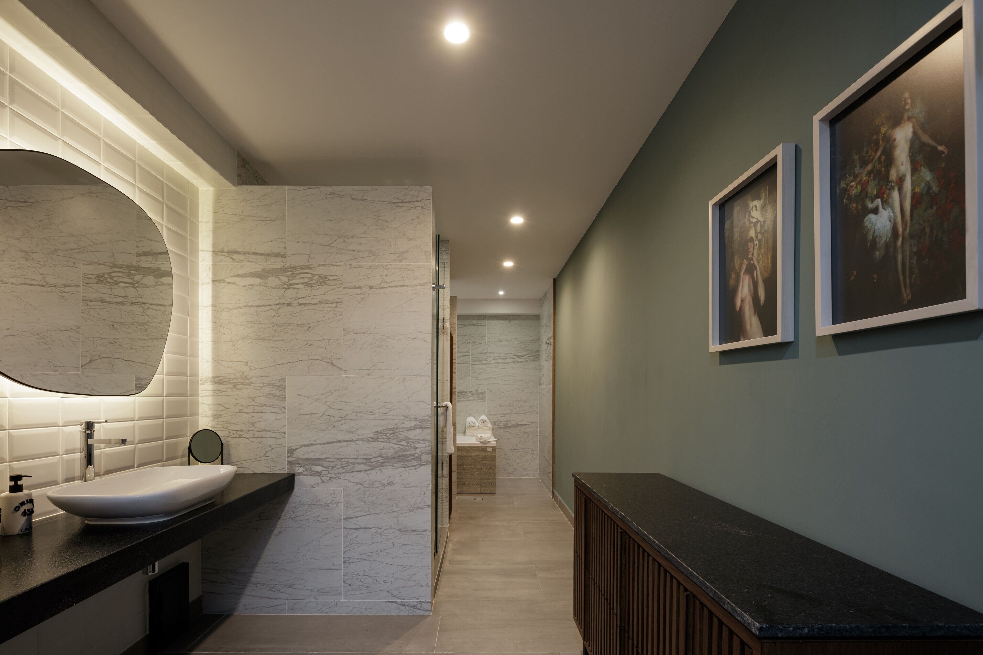 Un baño moderno con lavamanos de mármol, un espejo grande y obras de arte enmarcadas en la pared.