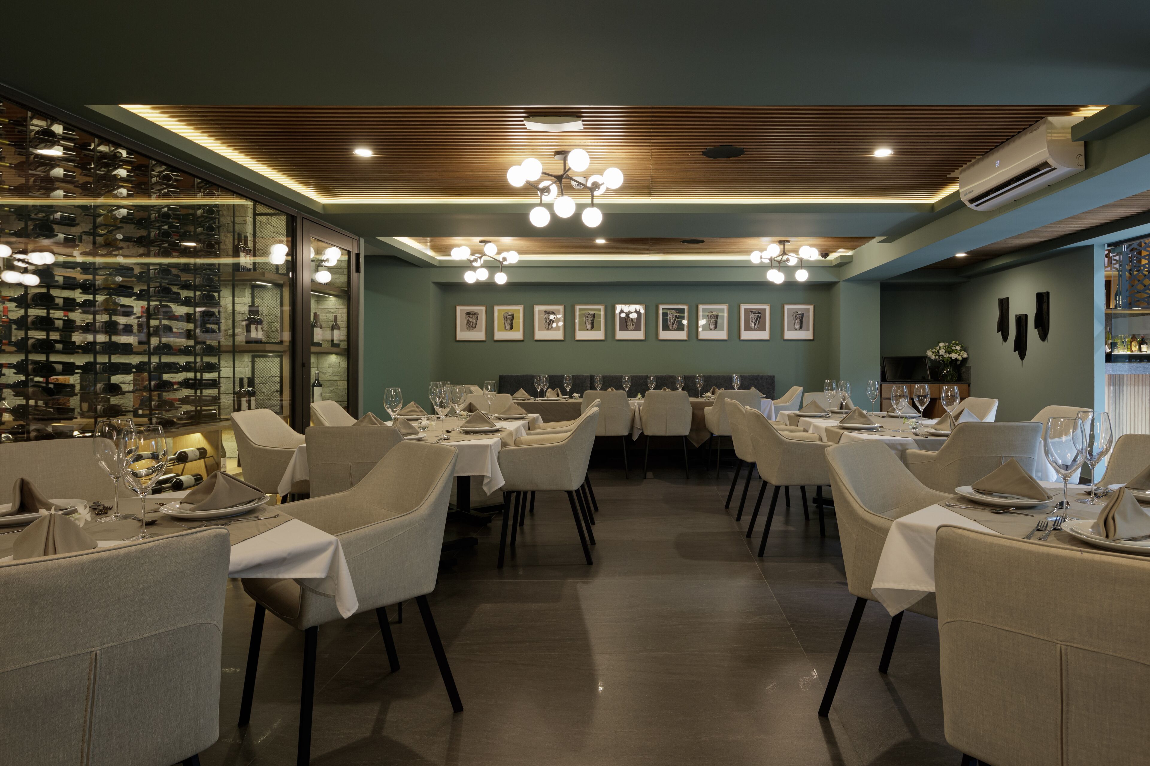 A restaurant with multiple tables set for dining, a wine rack, and framed pictures on the wall.