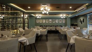 A restaurant with multiple tables set for dining, a wine rack, and framed pictures on the wall.