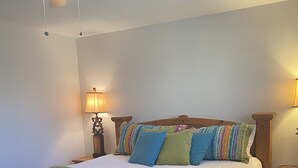 A wooden bed with a white comforter and colorful pillows, a ceiling fan, and two bedside lamps.