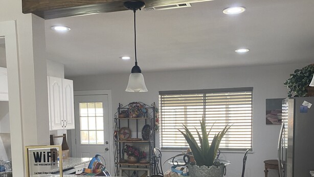 A kitchen with a central island, wooden chairs, a hanging light fixture, and a window with blinds.