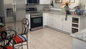 A modern kitchen with white cabinets, stainless steel appliances, a glass dining table, and colorful chairs.