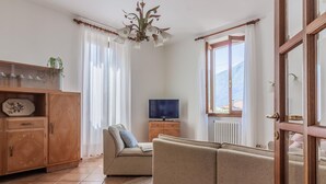 A living room with a sofa, television, wooden cabinet, and a view of mountains through the window. - Villa Gard by Wonderful Italy (Bellagio)