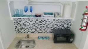 Cocina compacta con fregadero, microondas y salpicadero de azulejos.