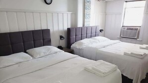 Habitación de hotel con dos camas, ropa de cama blanca, un reloj en la pared y una ventana con persianas.