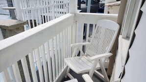 Un balcón exterior blanco con dos sillas Adirondack blancas y una jardinera de piedra.