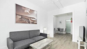 A modern interior with a grey sofa, a glass coffee table, a flat-screen TV, and a painting on the wall. - Modern Beachfront Suite 301 (Ocean City)
