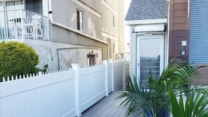 A balcony with a white fence, a potted plant, and a building with a number '405' on the door. - Modern Beachfront Suite 301 (Ocean City)