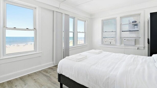 A bedroom with a bed, large windows, and a view of the beach. - Modern Beachfront Suite 301 (Ocean City)