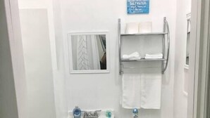 Ein kleines, kompaktes Badezimmer mit Toilette, Waschbecken und Spiegel. Über dem Waschbecken hängt ein Schild, und eine Handtuchstange mit Handtüchern ist vorhanden.