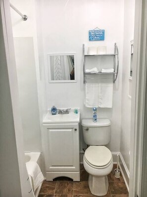 A small, compact bathroom with a toilet, sink, and a mirror. There is a sign above the sink and a towel rack with towels.