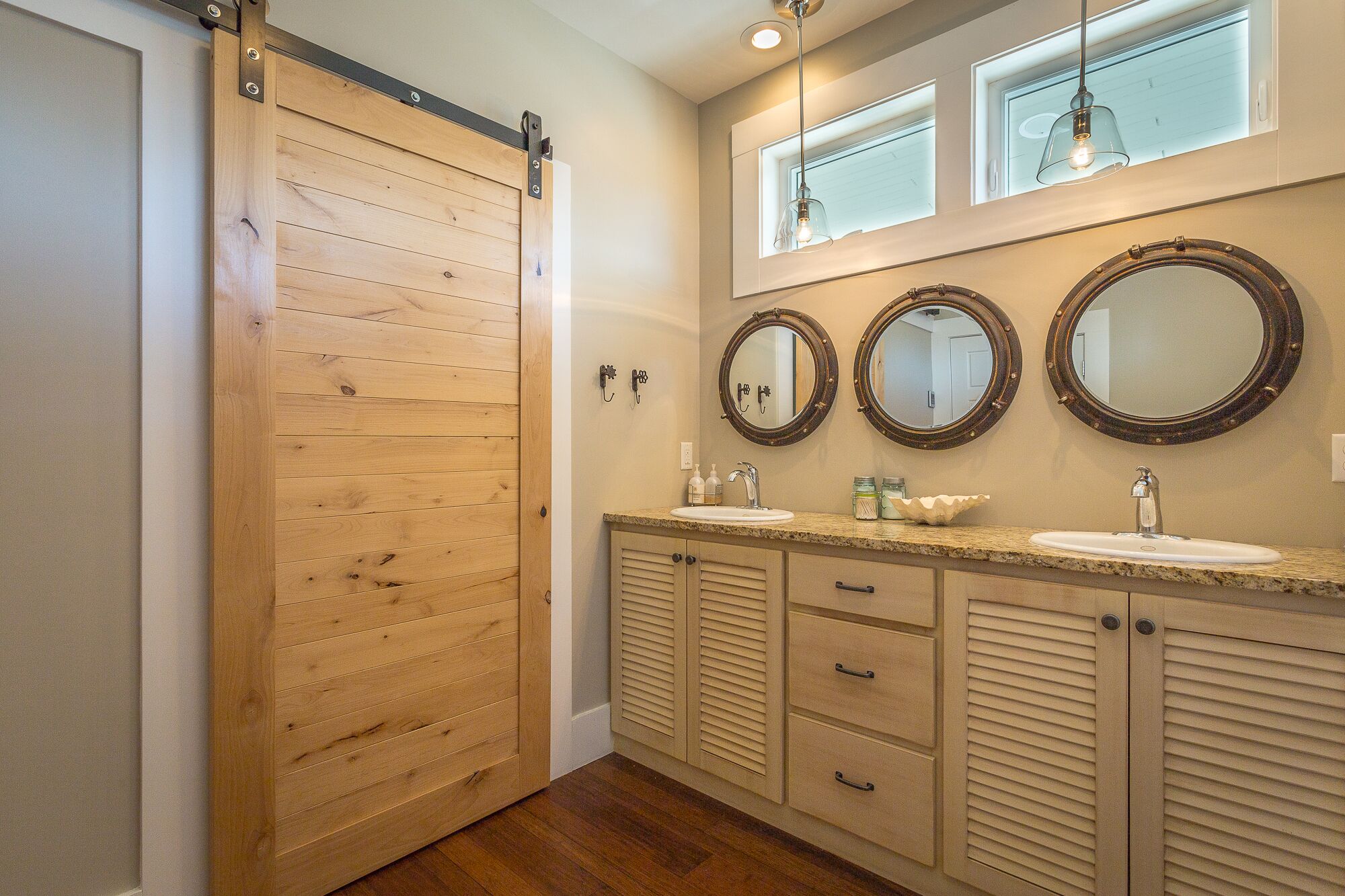 A bathroom with a wooden sliding door, two sinks with round mirrors, and a light fixture above the sinks.